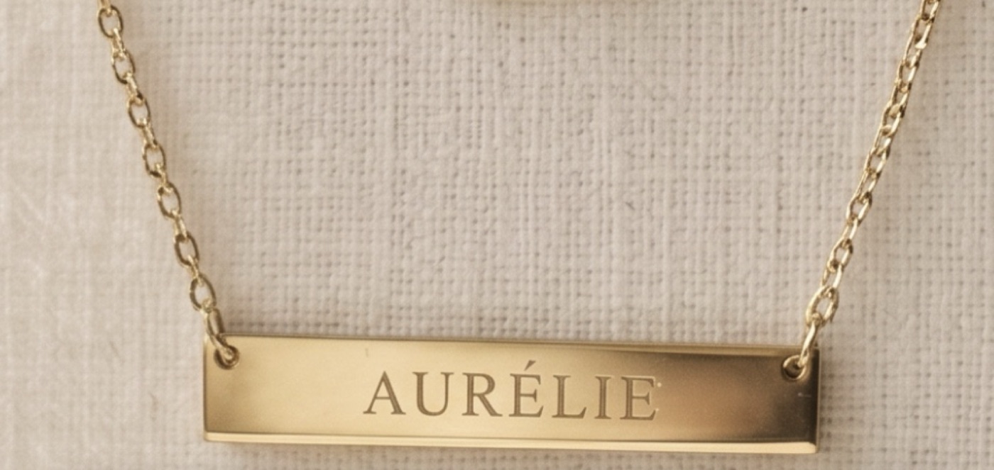 Product photo of a personalized gold bar necklace on a fabric background
