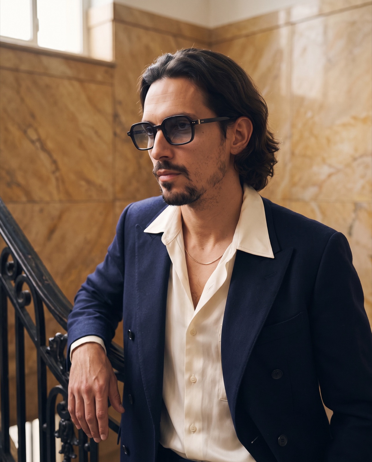Man in a navy blazer wearing square black glasses on a marble staircase