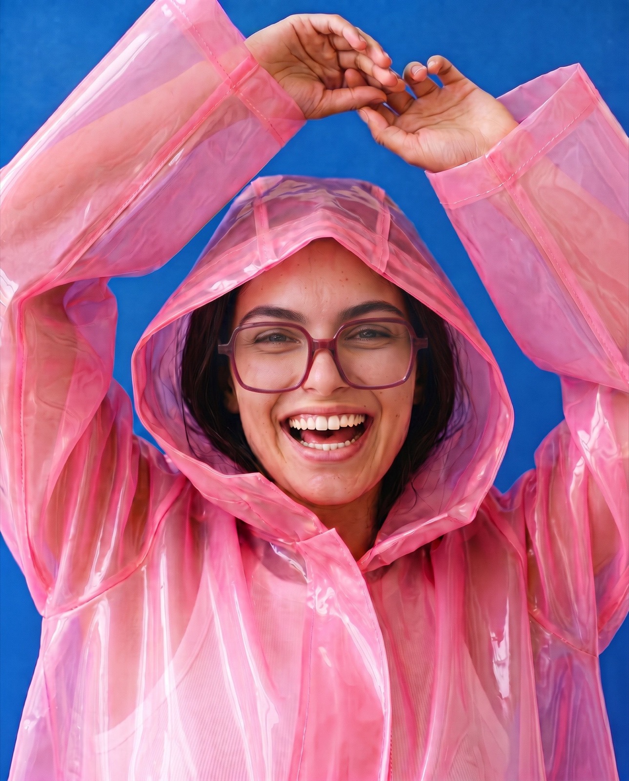 Woman in a pink raincoat laughing, wearing square glasses, colourful eyewear brand campaign