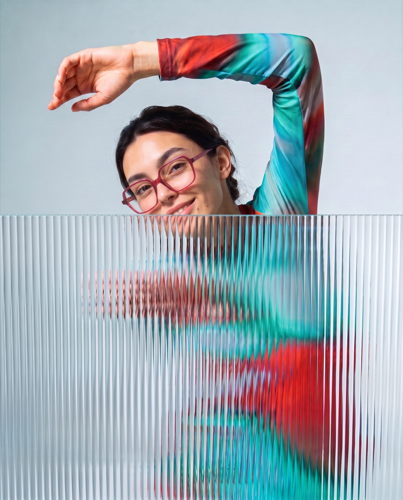 Woman peeking over a ribbed glass panel wearing red square glasses, colourful eyewear brand campaign