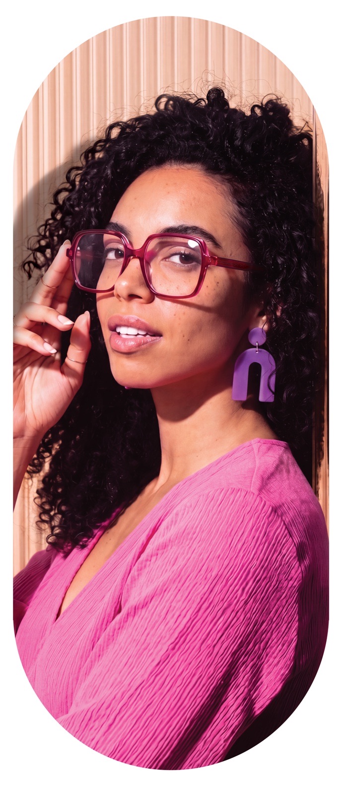 Woman with curly hair wearing pink square glasses, trade show wall portrait