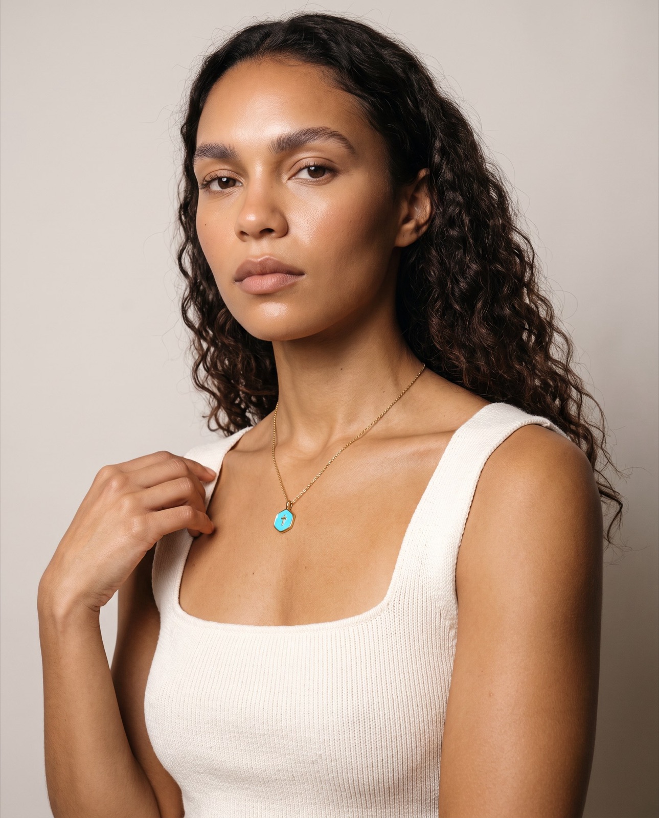 Model wearing a gold pendant necklace and a cream knit top