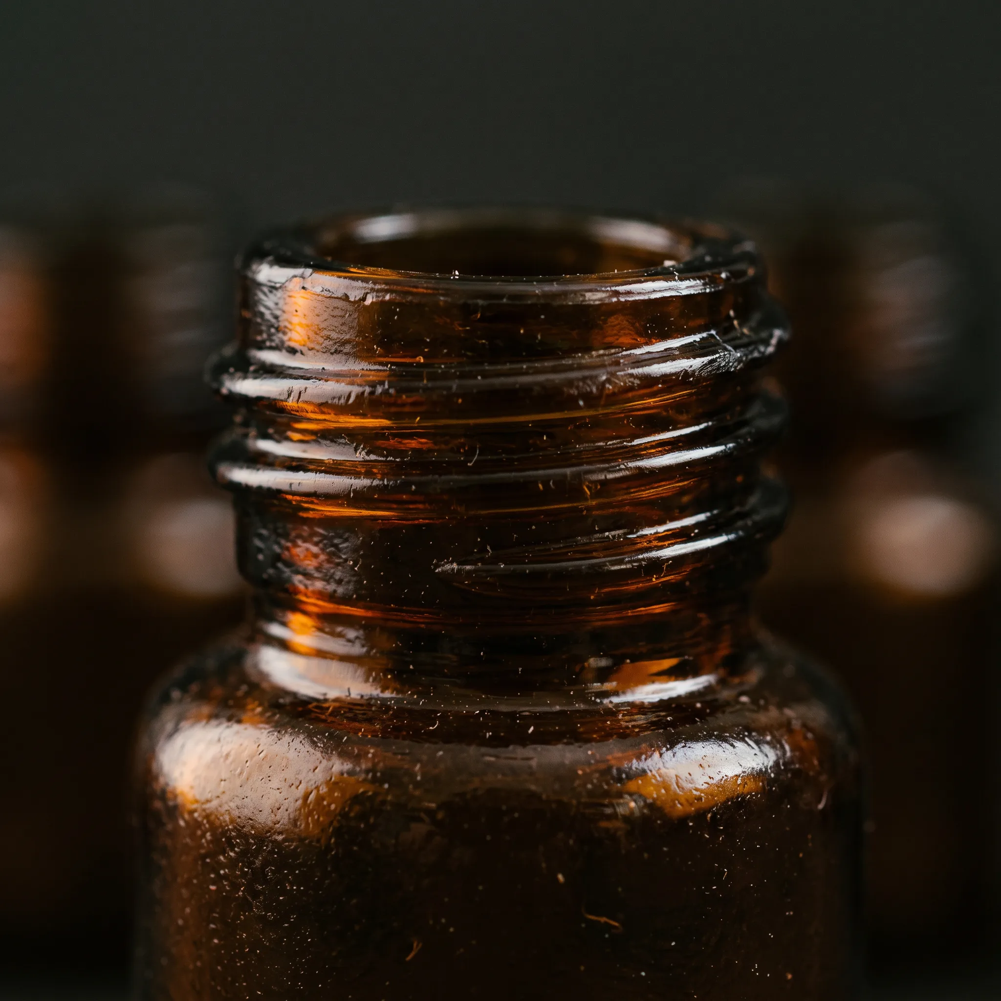 Macro detail of an amber glass bottle's threaded neck