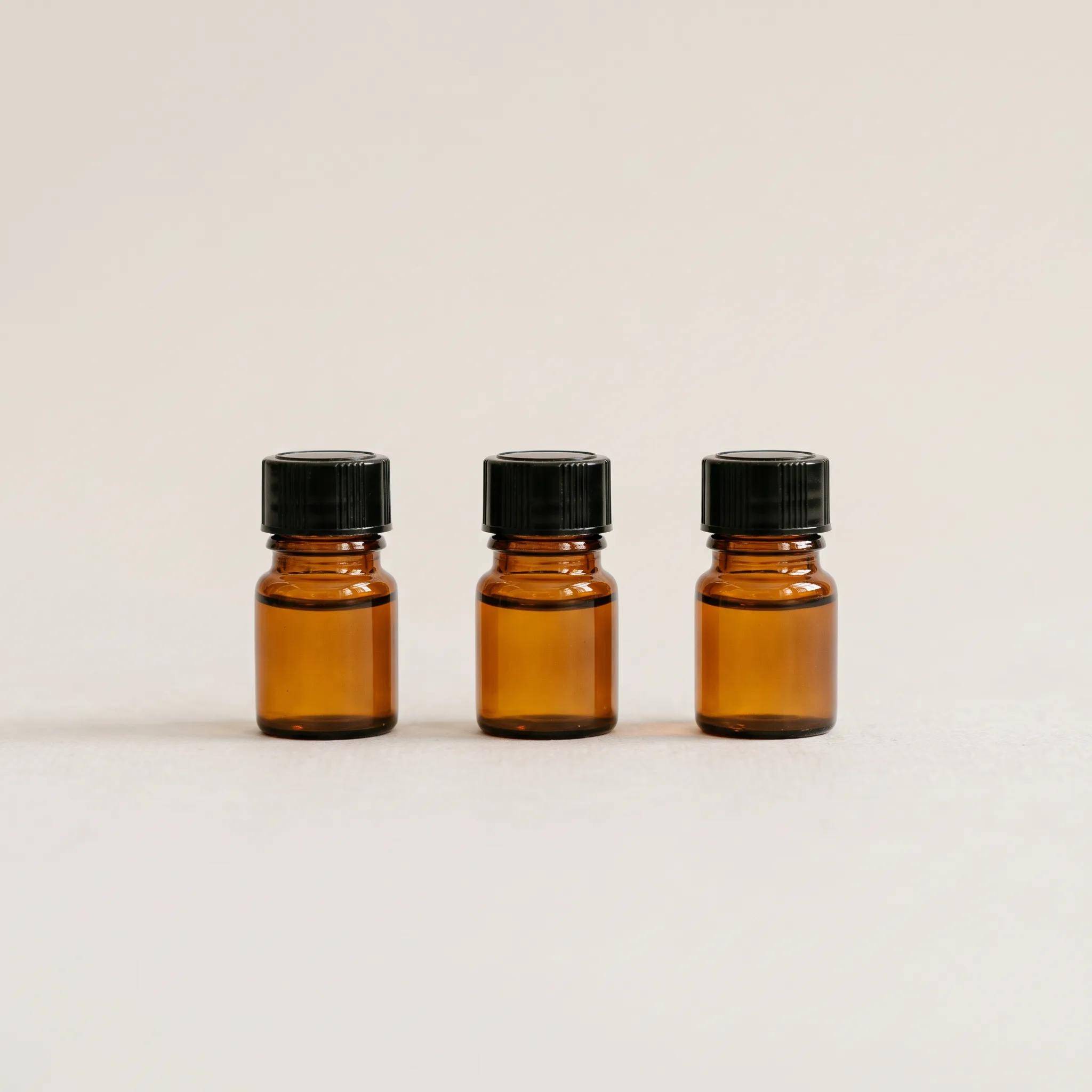 Three amber glass dropper bottles in a row on a seamless stone backdrop